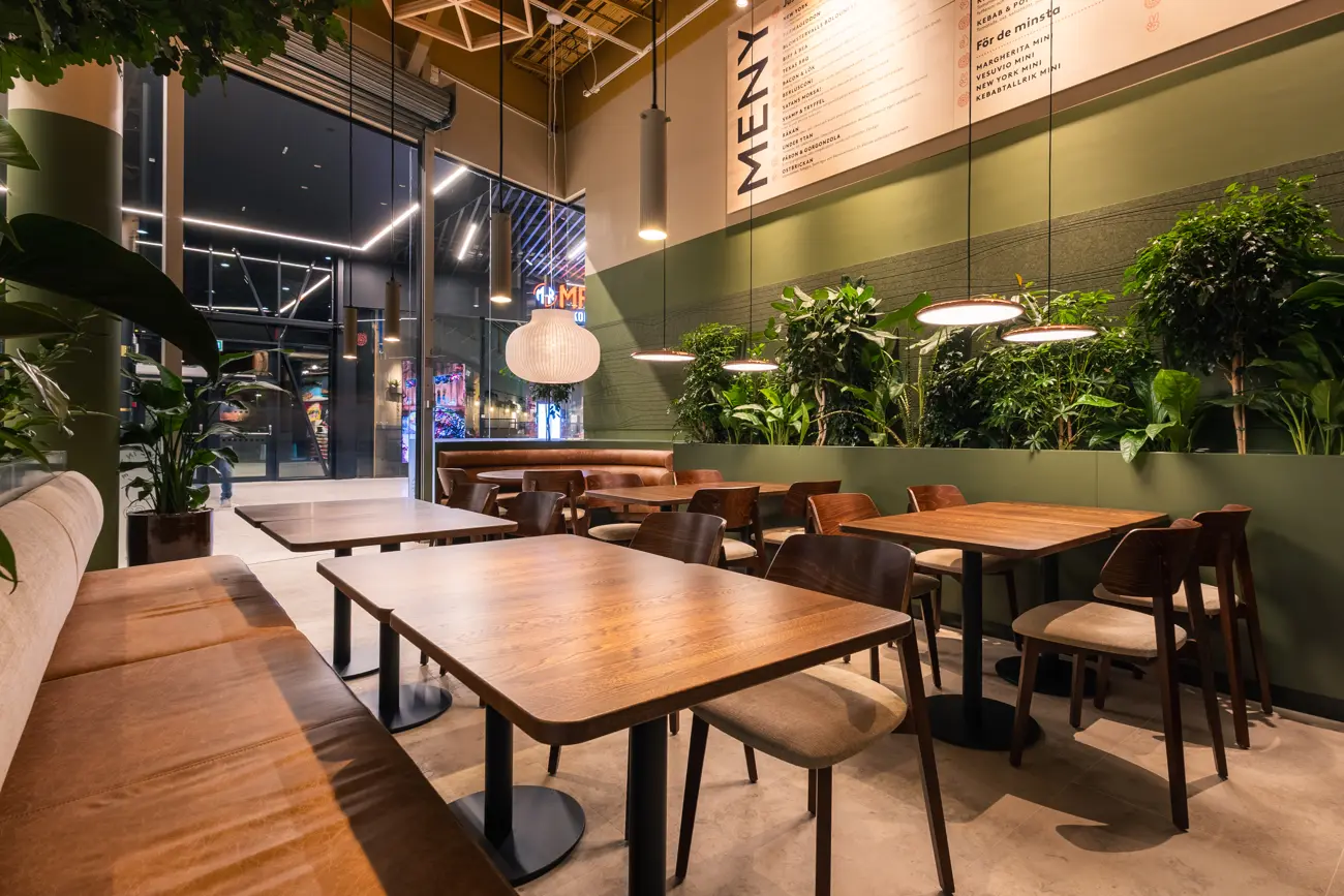 En Just In Time-restaurang med gröna växter, träbord och varm belysning
