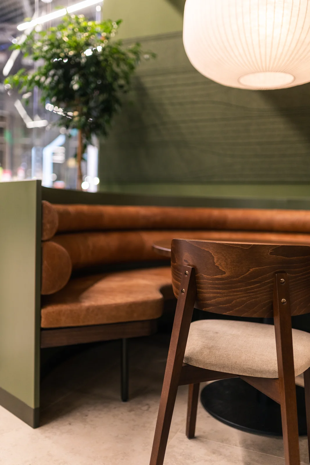 En sittplats med grön panel, brun soffa och en rund lampa.