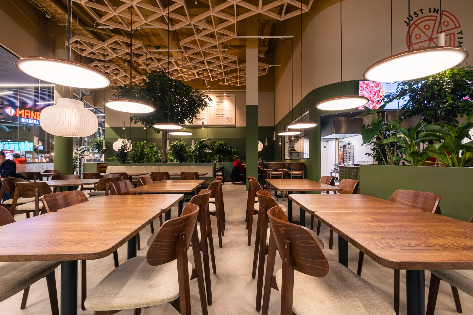 Dukningsfria träbord och stolar i restaurangen, med växter och runda taklampor.